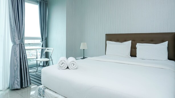 Ein Hotelzimmer mit einem großen Bett, zwei Kissen, einem Nachttisch mit Lampe, einem Sessel und Blick auf die Stadt durch das Fenster.