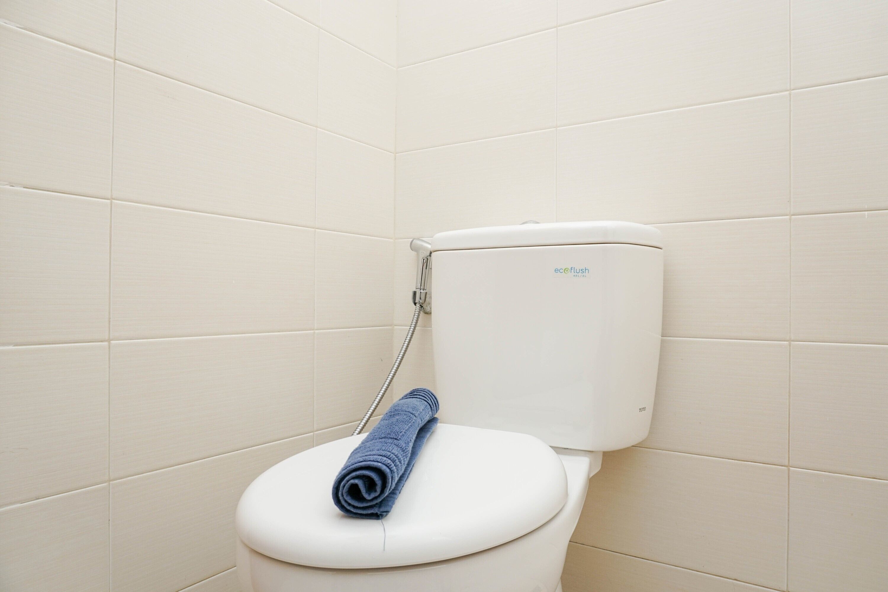 A toilet with a blue towel on the seat, a visible water tank, and a shower hose.