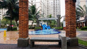 Una piscina con tobogán acuático, rodeada de palmeras y pilares de ladrillo.