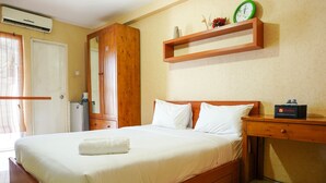 A neatly made bed with white linens, a wooden headboard, and a bedside table with a clock and a bottle. - Comfort Stay Studio Room @ Green Palace Kalibata Apartment (Jakarta)