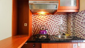 A compact kitchen with wooden cabinets, a gas stove, a kettle, and a sink. - Comfort Stay Studio Room @ Green Palace Kalibata Apartment (Jakarta)
