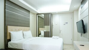 A modern hotel room with a large bed, a bedside table, a mirror, a TV, and a door. - Wonderful and Cozy Studio at Green Palace Apartment (Jakarta)