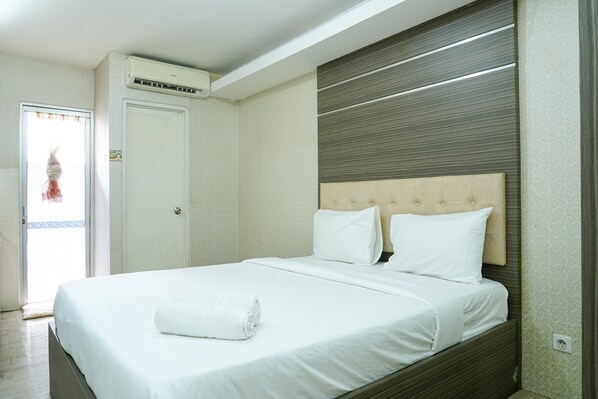 A hotel room with a bed, a window, and an air conditioning unit.
