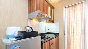 Una cocina compacta con estufa a gas, un lavamanos y armarios de madera. Una maleta de viaje y una cafetera están sobre la encimera.