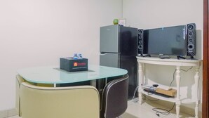 Una habitación compacta con una mesita de vidrio, un refrigerador, dos monitores y una caja Travelio.