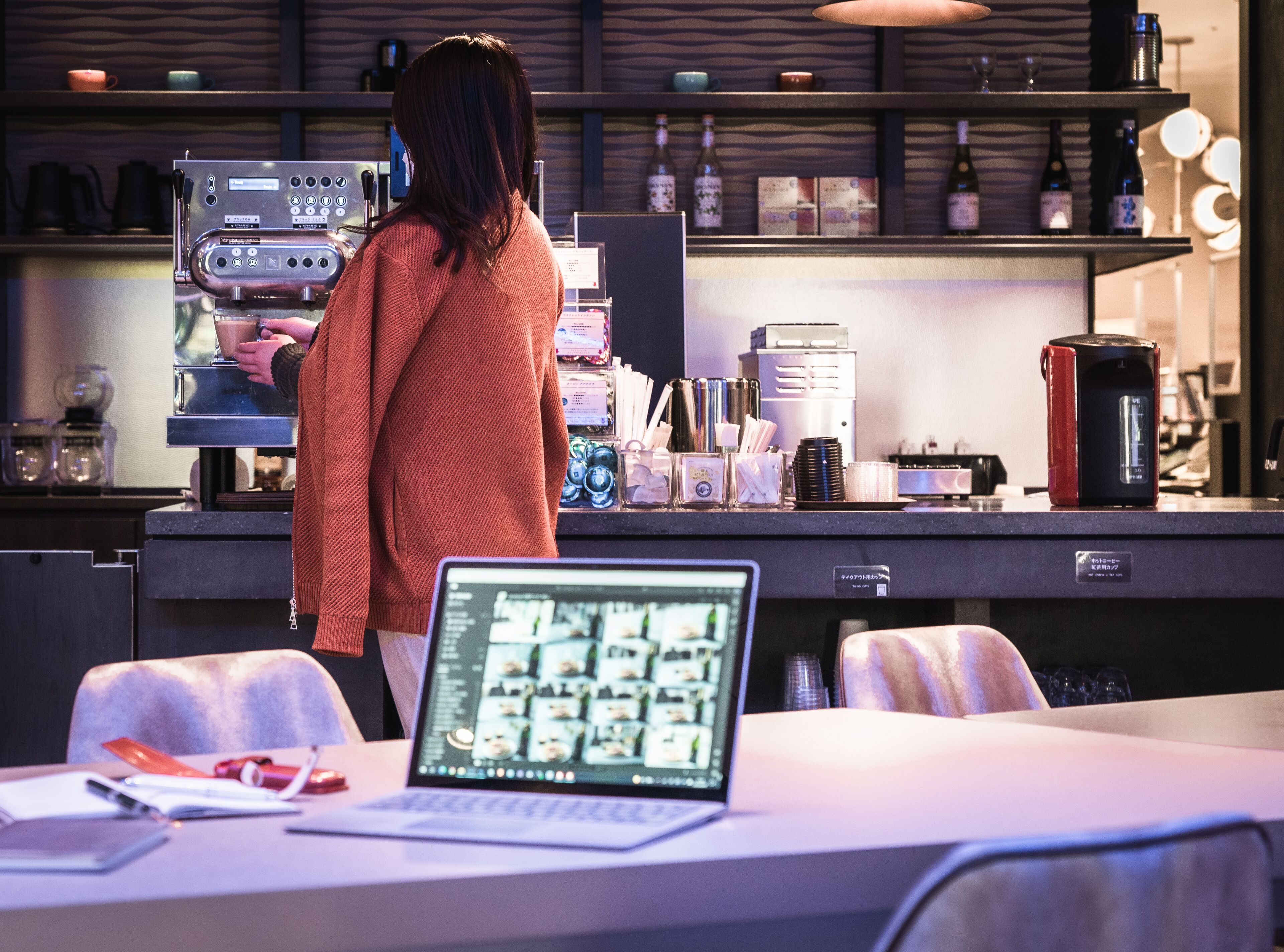 A bar area with a coffee machine, shelves with bottles, and a laptop on a table.