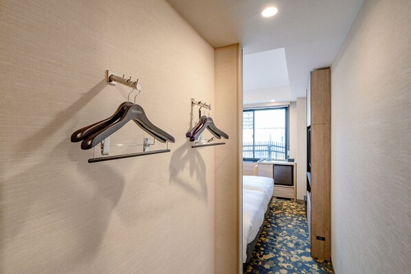 A hotel hallway with a bed, a window, and two wall-mounted coat racks.