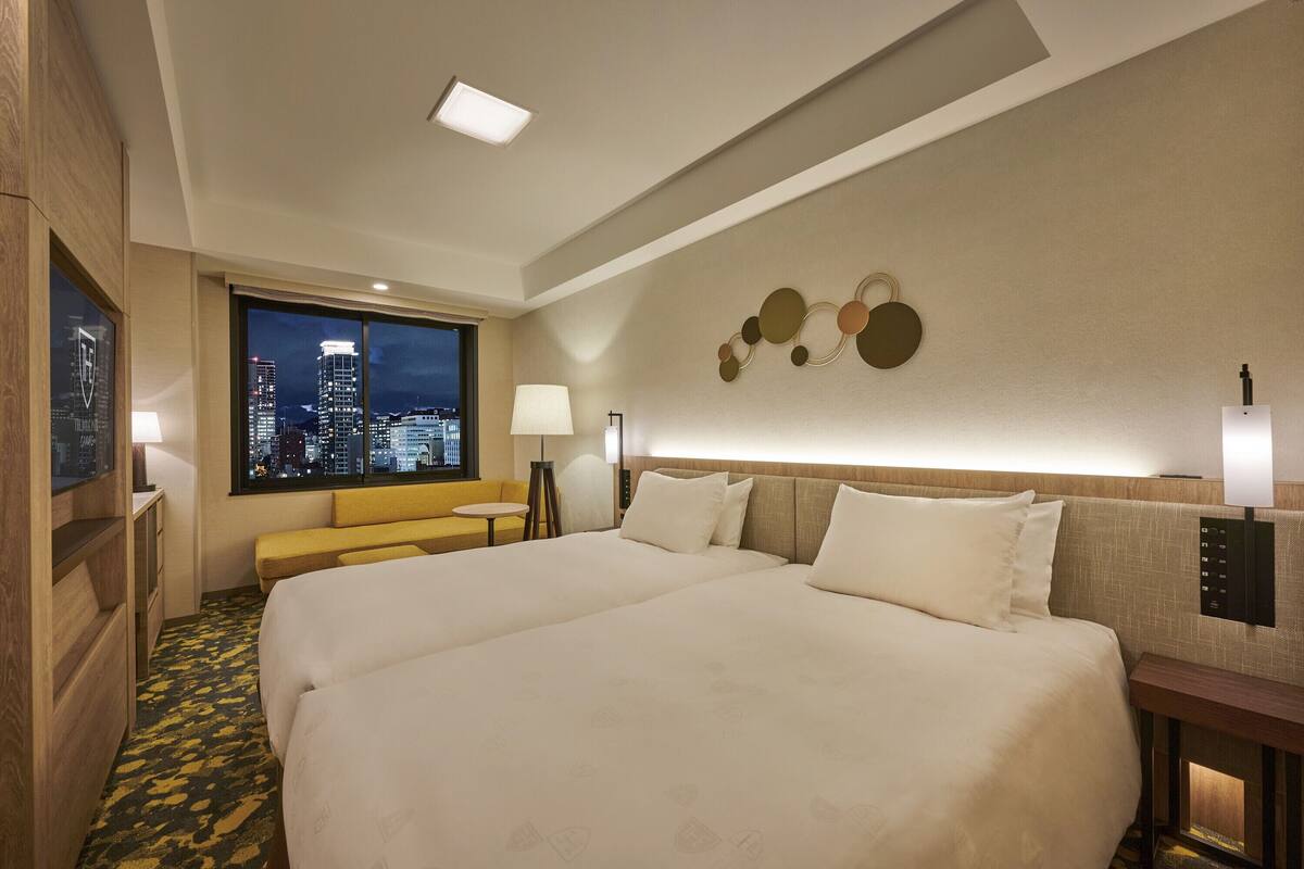 Habitación de hotel con una cama grande, un sofá, un escritorio y vistas a la ciudad.