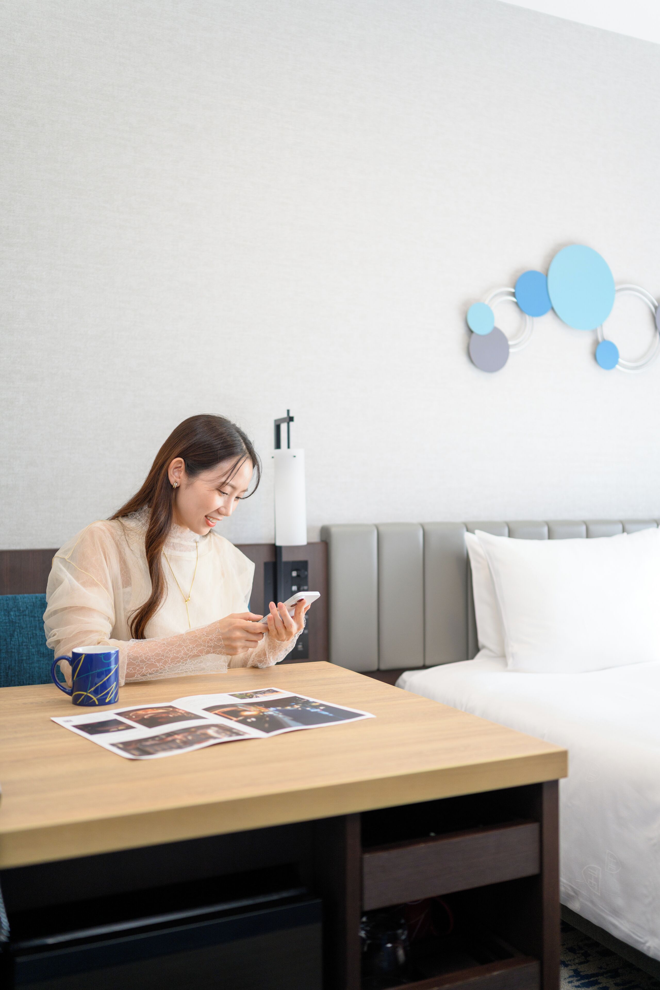 A hotel room with a bed, a bedside table with a coffee mug, a lamp, and a wall decoration.