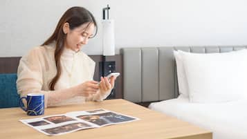 A hotel room with a bed, a bedside table with a coffee mug, a lamp, and a wall decoration.