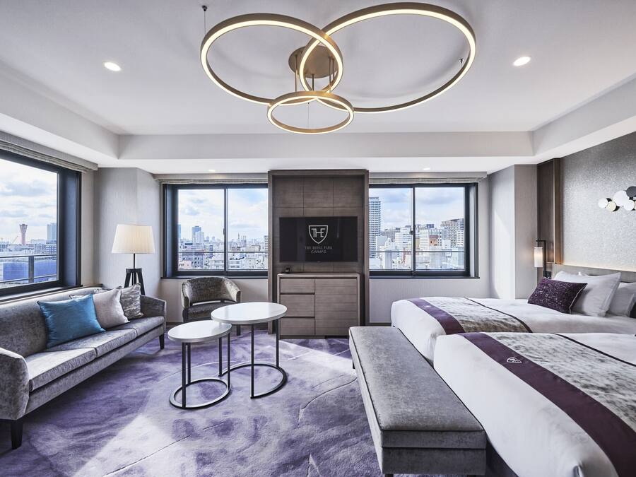 A modern hotel room with a city view, a sofa, a bed, a small table, and a TV.