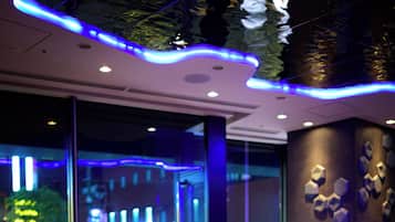 Un espacio interior moderno con mesas, sillas, ventanas amplias y decoración en las paredes.