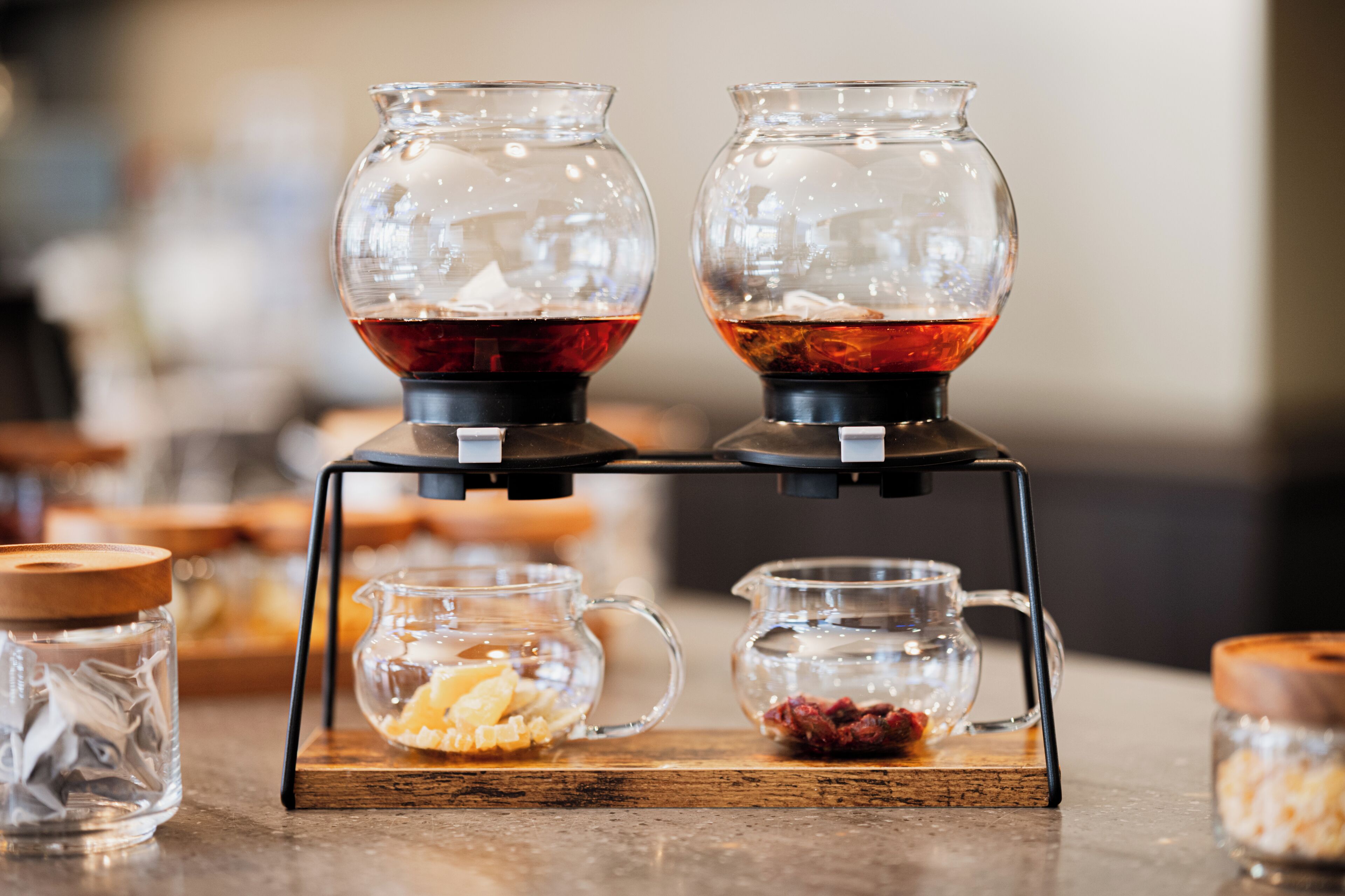 A coffee station with two glass carafes, a small pitcher, and a container with nuts and dried fruit.