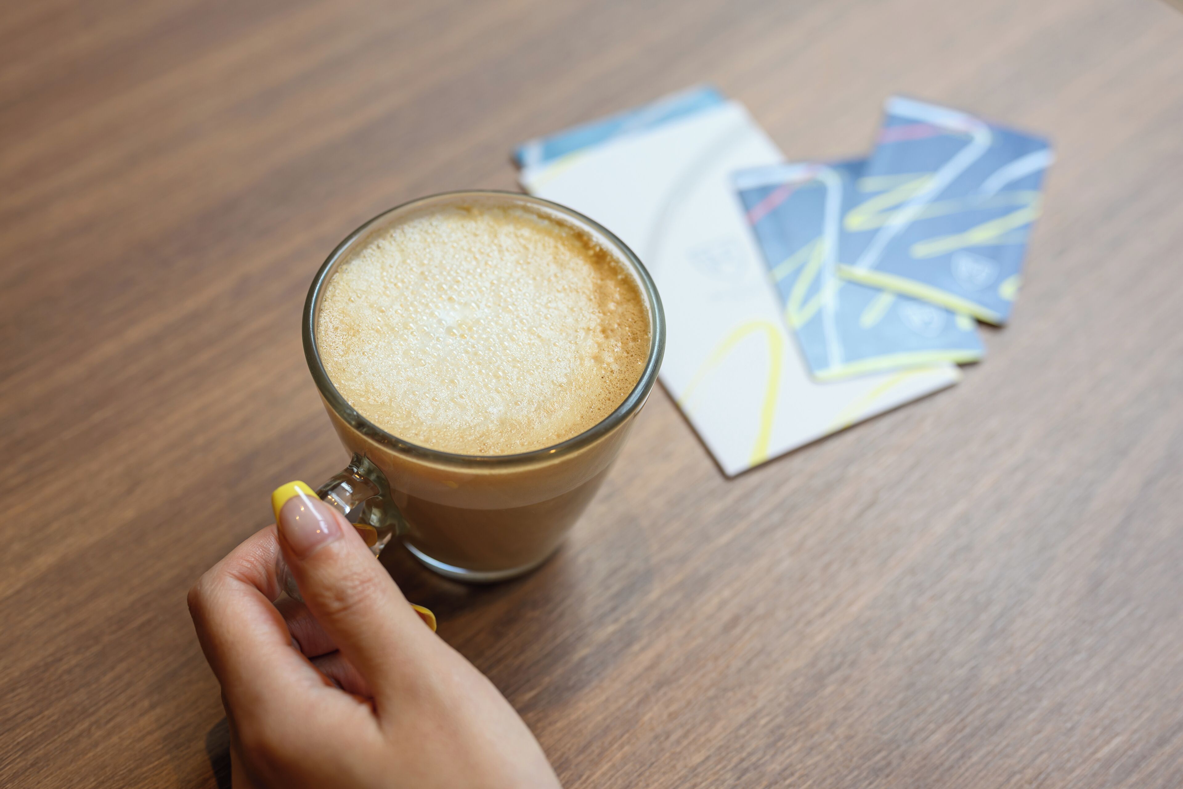 Una mano sostiene una taza de café sobre una mesa de madera con cartas de juego.