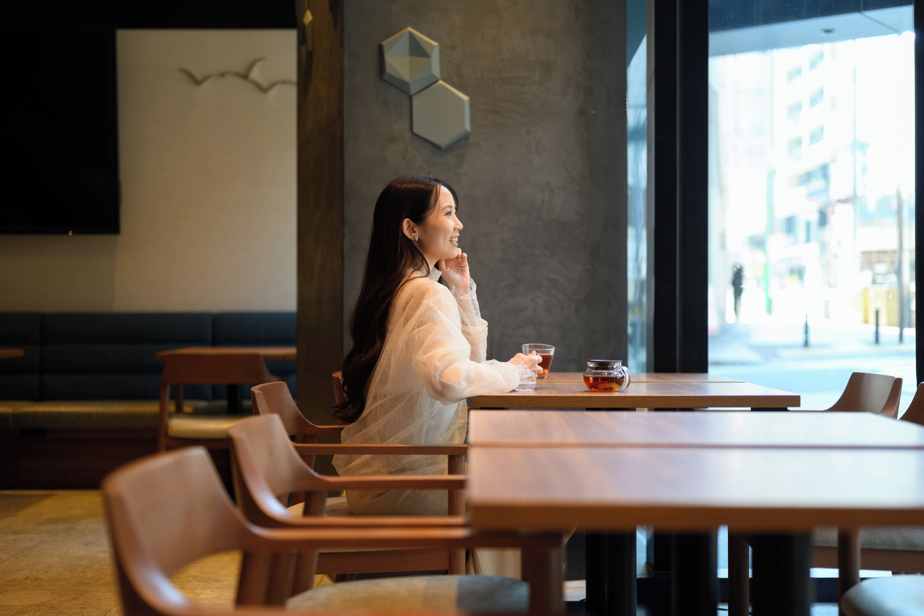 Une femme est assise à une table en bois dans un café, d’où elle a vue sur la rue.