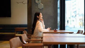 Une femme est assise à une table en bois dans un café, d’où elle a vue sur la rue.