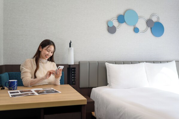 Una habitación de hotel con cama, mesita de noche, lámpara y una obra de arte en la pared.