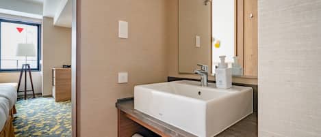 A hotel bathroom with a large white sink, a mirror, and a towel rack.