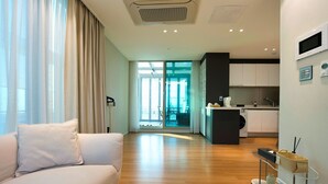 A modern living room with a sofa, a glass door leading to a balcony, and a kitchen area with cabinets and a microwave. - K-Hills The Terrace (Paju)