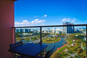 A balcony with a table and chairs, overlooking a cityscape with high-rise buildings and a river.