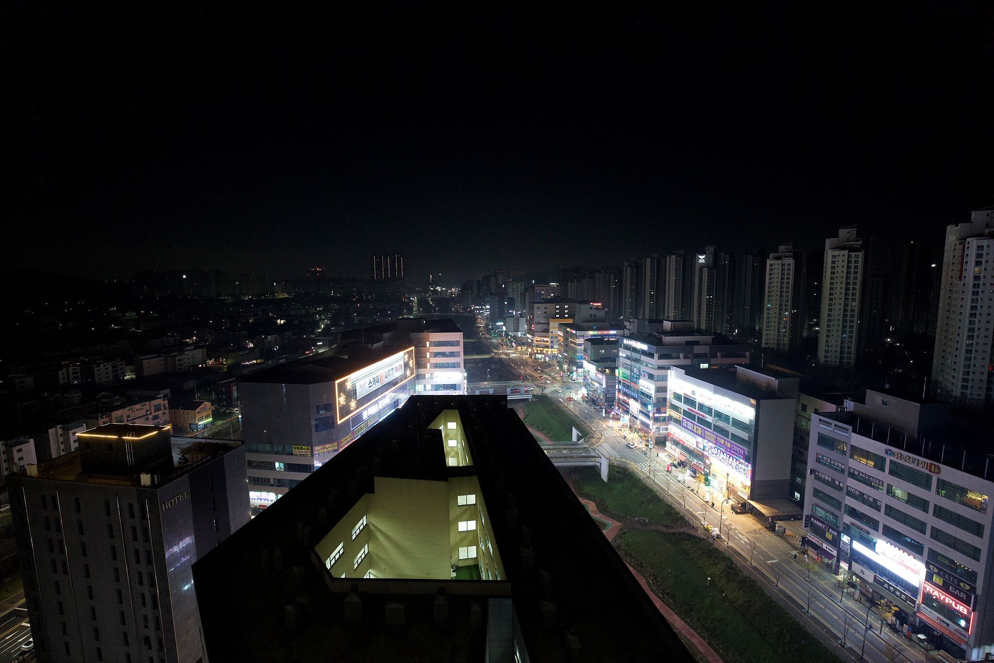 Un edificio de gran altura con varios pisos, una terraza en la azotea y una planta baja bien iluminada con señalización visible.