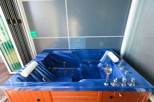 Una bañera de hidromasaje azul con base de madera, una placa en la pared y una ventana con persianas.