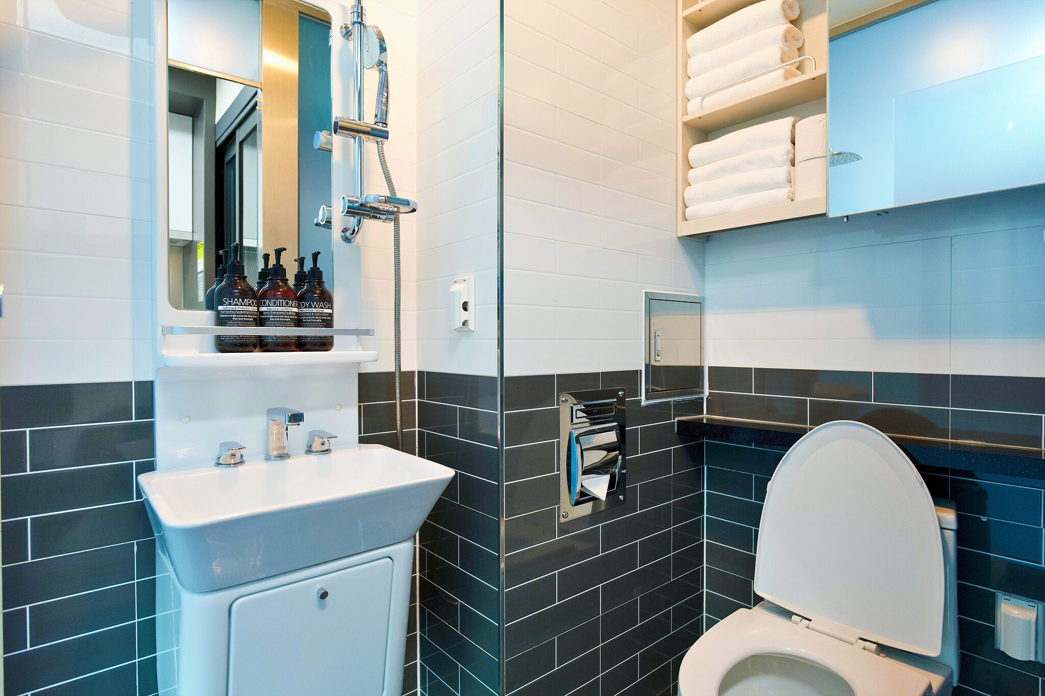 A modern bathroom with a white sink, a mirror, a shower, and a toilet.
