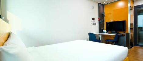 Una habitación de hotel con una cama, un escritorio con una computadora y un televisor.