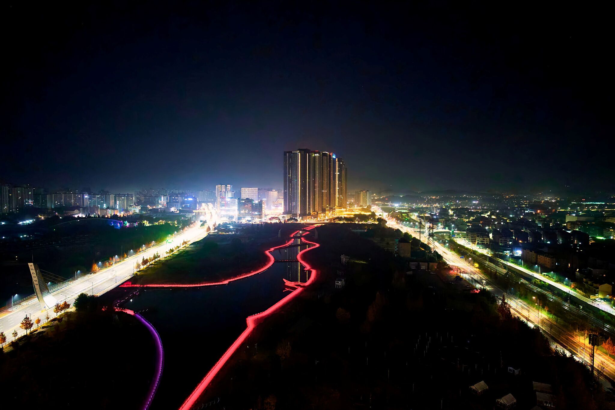 Paisaje urbano nocturno con edificios iluminados, un río y un puente.