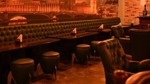 A bar with leather booths and stools, a brick wall, and a cityscape mural in the background. - Hotel MD's Continental (East Jorhat)