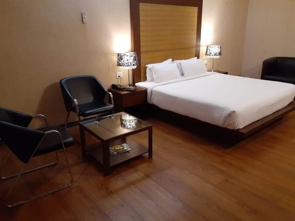 A hotel room with a bed, a chair, a nightstand, a lamp, and a small table.