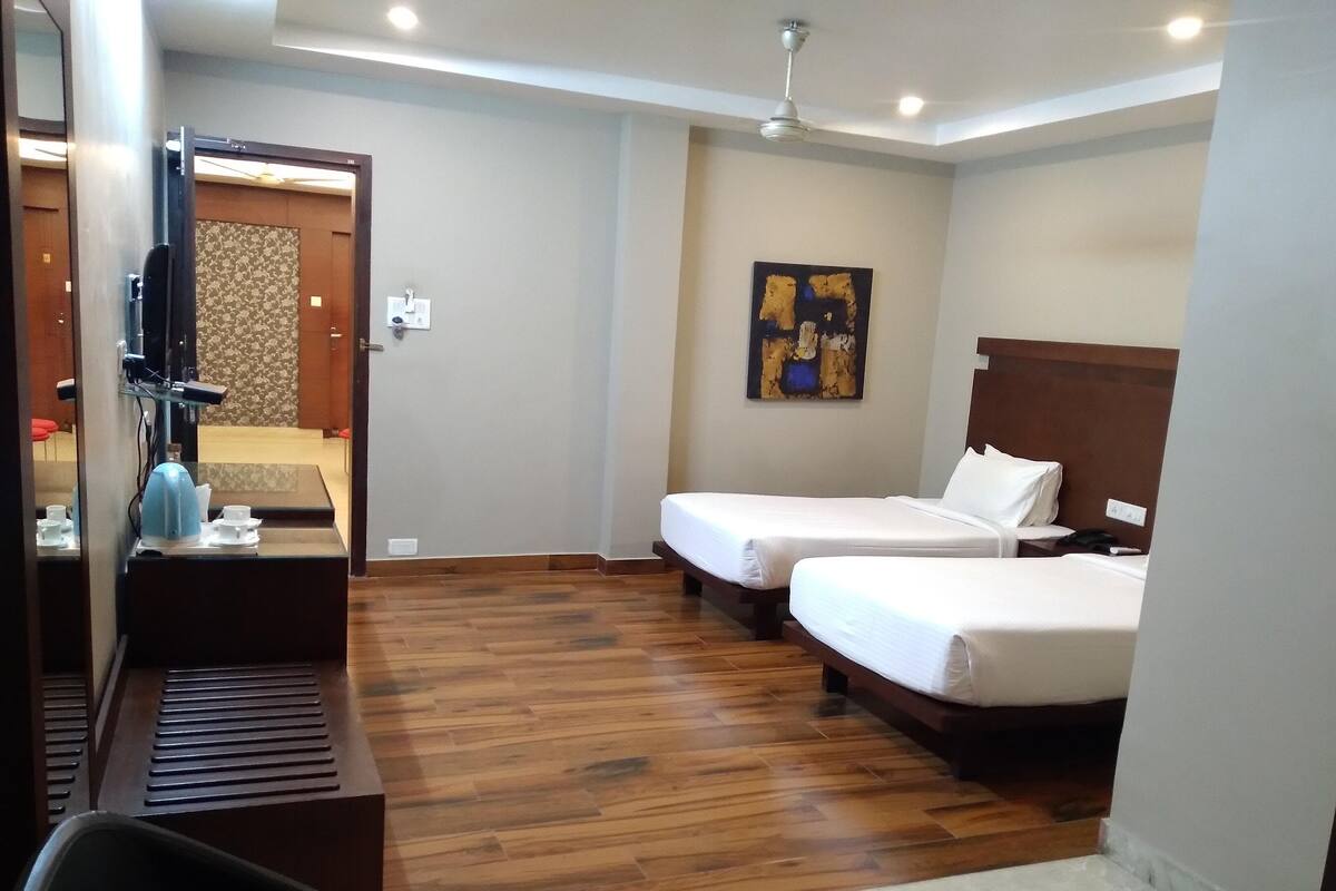 A hotel room with two beds, a desk with a chair, a ceiling fan, and a painting on the wall.
