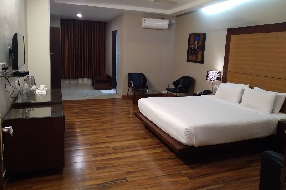 A hotel room with a large bed, a desk with a mirror, a chair, a lamp, and an air conditioning unit.