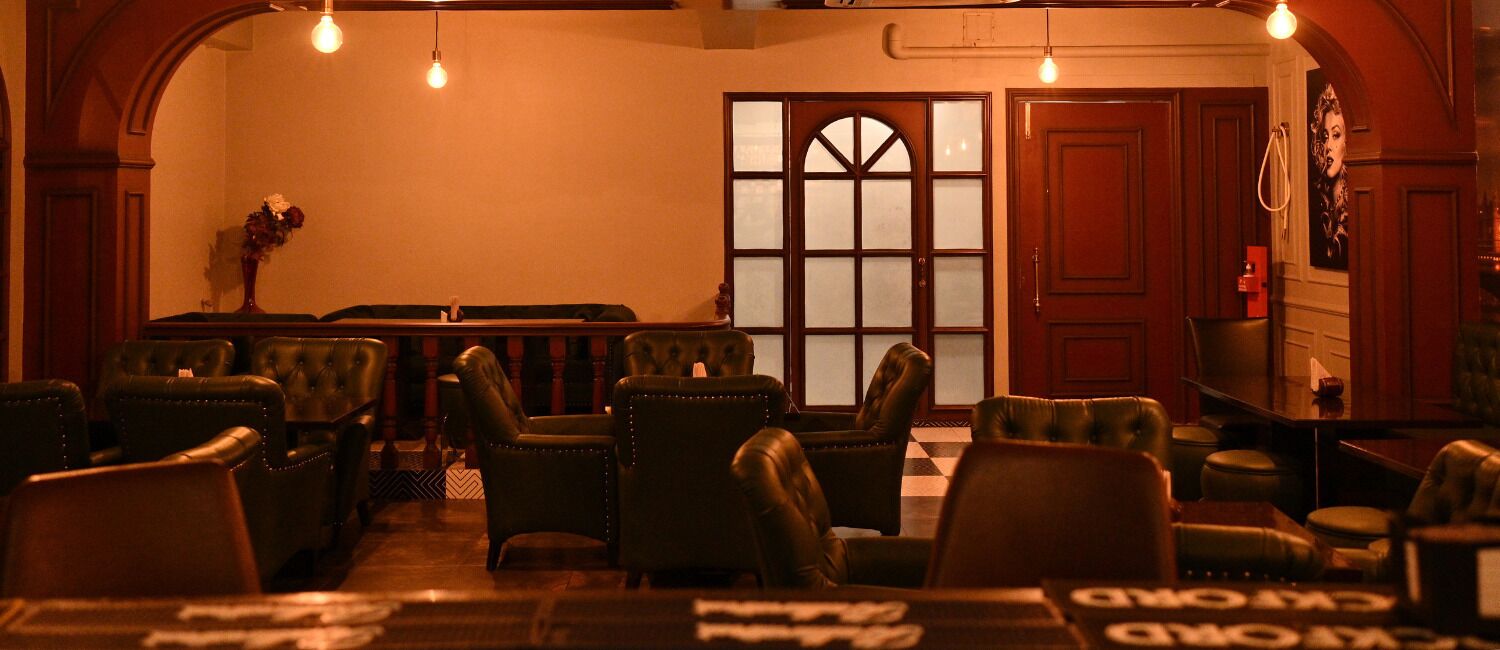 Una zona de bar con sillones de cuero y mesas, un amplio ventanal de arco y una puerta con paneles de vidrio satinado.