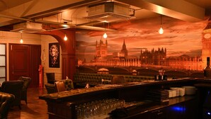 A bar with a view of a city skyline, leather seating, and a red door. - Hotel MD's Continental (East Jorhat)