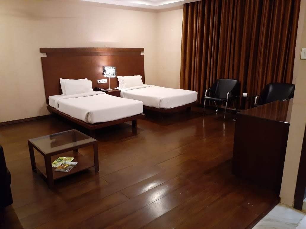 A hotel room with two beds, a desk, a chair, and a small table with a magazine.