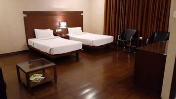 A hotel room with two beds, a desk, a chair, and a small table with a magazine.