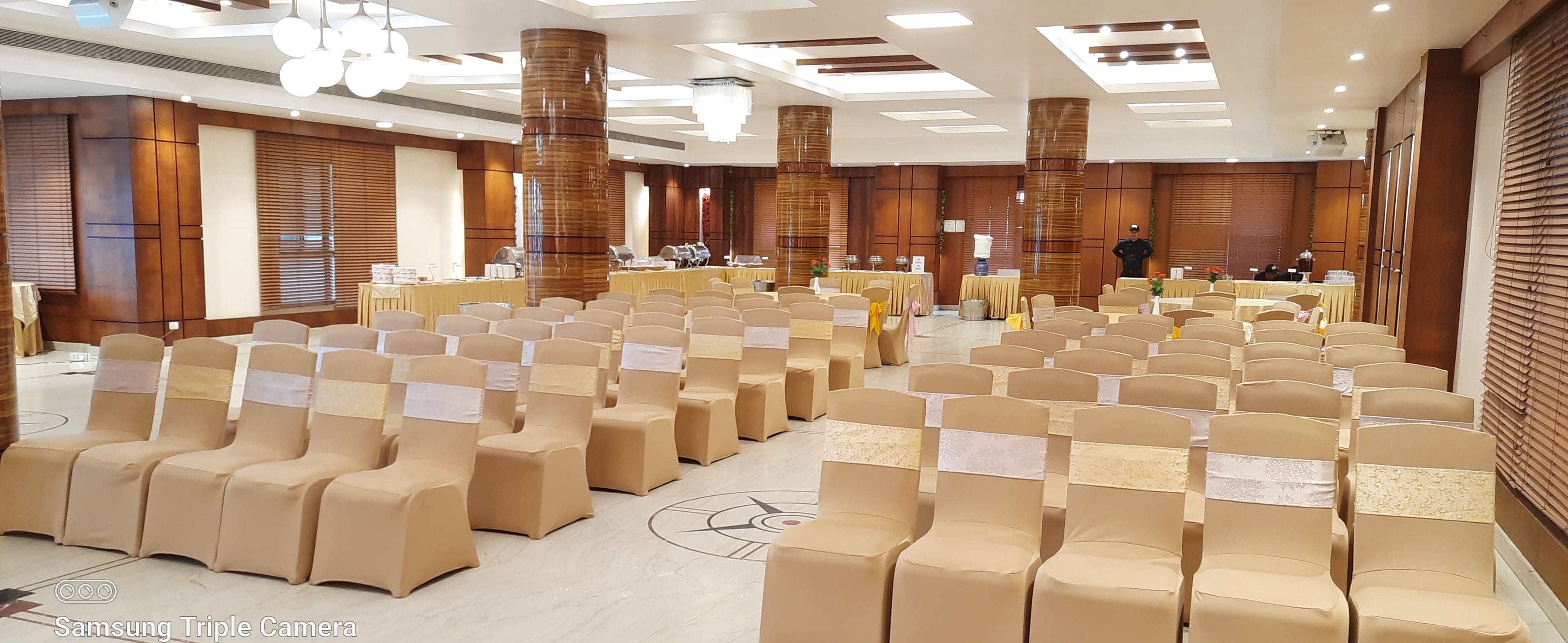 Un salón de conferencias con filas de sillas color beige, un escenario con un atril y una gran lámpara de araña.