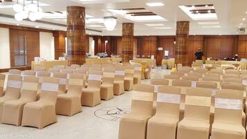 Un salón de conferencias con filas de sillas color beige, un escenario con un atril y una gran lámpara de araña.