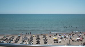Een strand met rijen ligbedden en parasols, een heldere lucht en de oceaan op de achtergrond.
