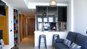 Een moderne keuken met een centraal eiland, een zithoek met een bank en krukken, en een hal met een kleurrijk opbergmeubel.