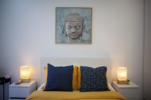 Een slaapkamer met een bed, twee nachtkastjes met lampen en een boeddhabeeld aan de muur.