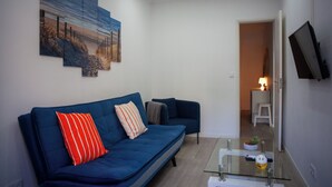 A modern living room with a blue sofa, a glass coffee table, and a flat-screen TV mounted on the wall. - Just4u Apartment - Near Lisbon & Beach - With AC (Almada)