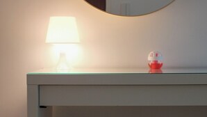 A white console table with a round mirror above it, a small lamp on the table, and a woven basket underneath. - Just4u Apartment - Near Lisbon & Beach - With AC (Almada)