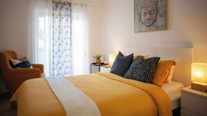 A hotel room with a large bed, a chair, a nightstand, and a Buddha painting on the wall. - Just4u Apartment - Near Lisbon & Beach - With AC (Almada)