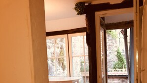 A room with a wooden floor, a white table, and a view of a stone building through a window. - W.1. Ruhiges Apartment mit Veranda am Schlossgarten (Hirschhorn (Neckar))