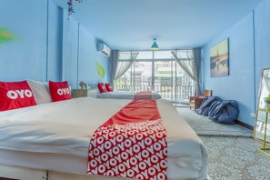Hotelkamer met een groot bed, rode en witte kussens, een gestreept plaid, een raam met gordijnen en uitzicht op de stad.