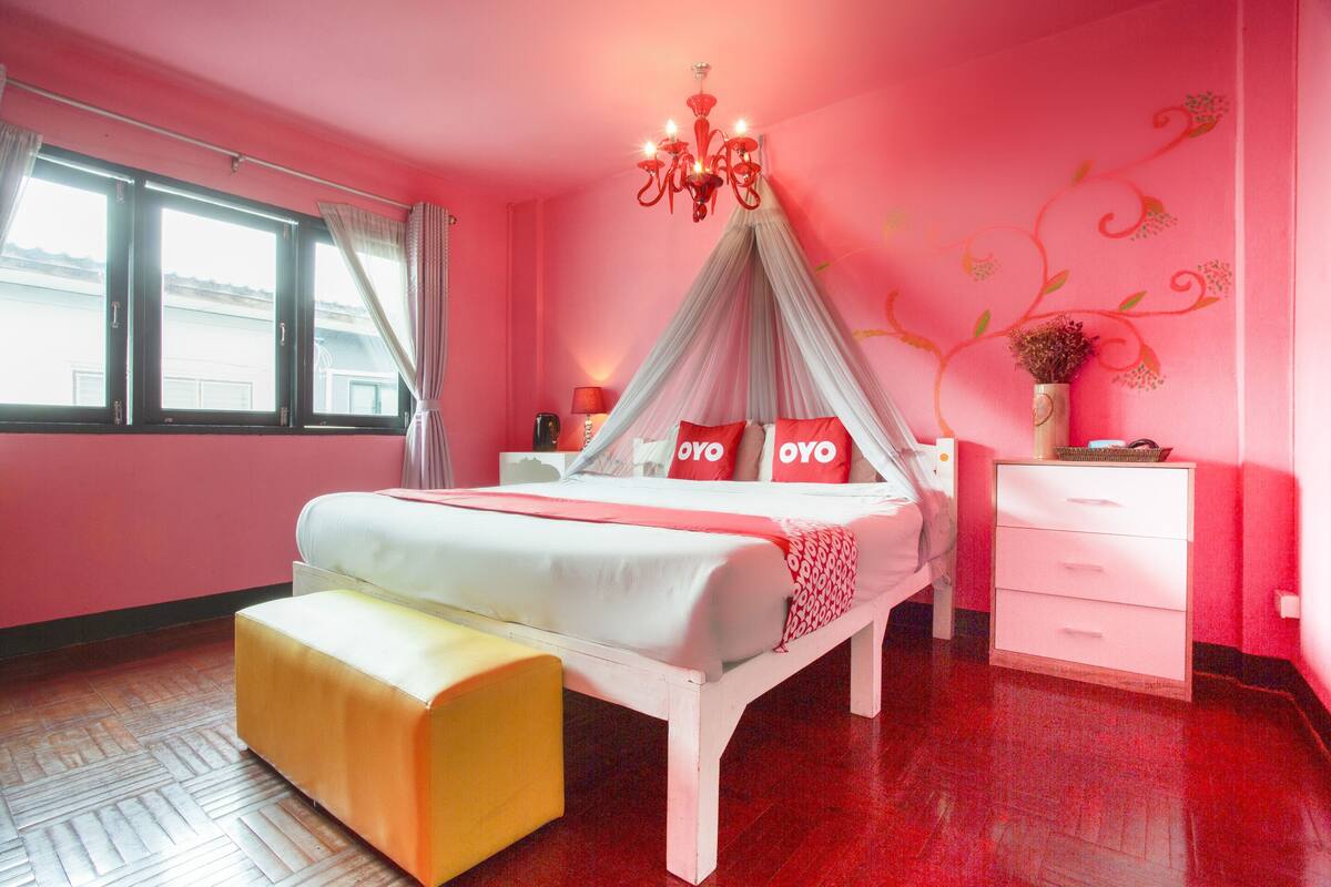 Une chambre à coucher décorée dans des tons de rose, avec un lit à baldaquin, une table de chevet, une commode, un banc et une coiffeuse.