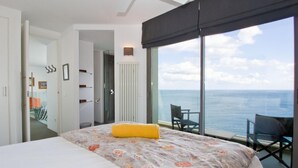 Een hotelkamer met een bed, uitzicht op zee en een balkon met stoelen.