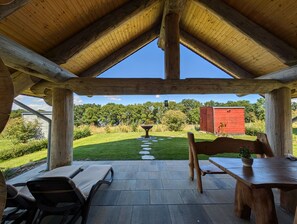 A covered patio with a view of a green lawn and a red shed.